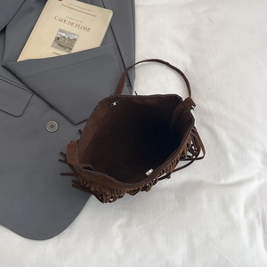 Sac à bandoulière rétro en daim marron avec franges et fermeture magnétique sur fond blanc