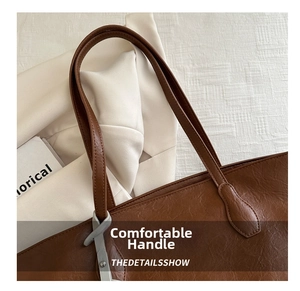 Close-up of brown tote bag showing leather texture, stitching and metallic hook