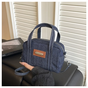 Detail of dark blue denim handbag featuring contrast stitching and leather patch decoration