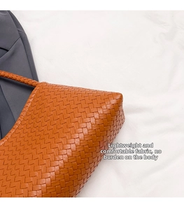 Detail shot of the woven texture and bottom structure of an orange shoulder tote bag
