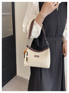 Detail of beige fabric dumpling bag with dark brown leather trim and beaded ornament