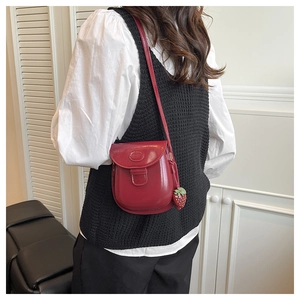 Detail of red glossy leather crossbody bag with strawberry pendant and metallic emblem
