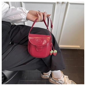 Gros plan du sac besace rouge brillant avec pendentif fraise et écusson logo ovale