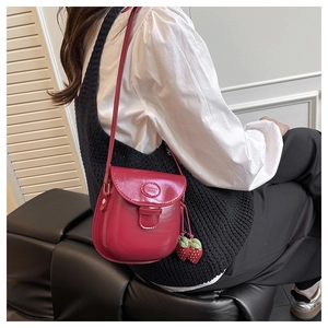 Detail of red leather crossbody bag with strawberry charm worn by model on shoulder