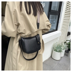 Detail of black pebbled leather crossbody bag featuring stylish wide woven shoulder strap
