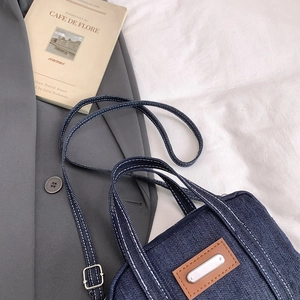 Blue denim crossbody pillow bag with white contrast stitching and brown leather patch details