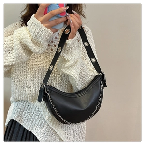 Detail of a black hobo bag with silver chain and eyelet straps held by a model