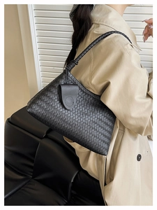 Detail of black woven shoulder bag showing premium texture and knot strap on trench coat