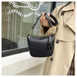 Close-up of black leather bucket bag with gold hardware and tassel charm in a cafe setting