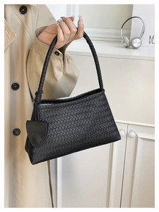 Close-up of black woven leather tote bag with braided handle and small round accessory