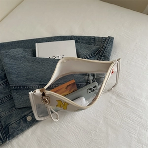 Transparent PVC handbag with embroidered letter N and white trim shown with daily essentials