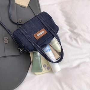 Blue denim mini pillow crossbody bag with leather patch and zip closure on grey blazer