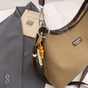 Sac hobo en toile kaki avec bordure en cuir et breloque en perles sur fond neutre