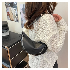 Detail of a black hobo bag with silver chain worn over a white knit sweater