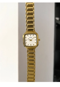 Détail d'une montre carrée dorée avec bracelet en acier poli et guichet de date