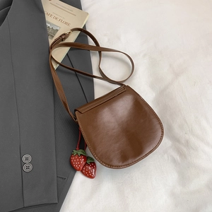 Sacoche selle marron vintage avec breloque fraise sur tissu blanc et magazine
