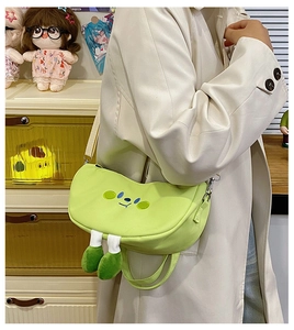 Detail of green cartoon half-moon crossbody bag with embroidered face and plush feet