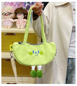 Close-up of green canvas half-moon bag with cute cartoon embroidery and plush leg charms