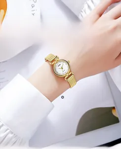 Detail of gold mesh strap ladies watch with diamond markers next to coffee cup