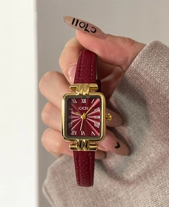 Dettaglio di un piccolo orologio rettangolare dorato con cinturino in pelle rossa al polso