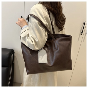 Detail of large dark brown leather tote bag with charm accessory worn by female model