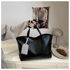 Detail of a large black tote bag with wrinkled leather texture on a white cabinet