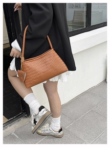 Detail of a brown woven leather tote bag with round braided handles and side charm detail