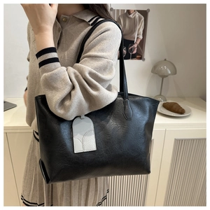 Detail of a black leather tote bag with pleated texture and stylish side tag accessory
