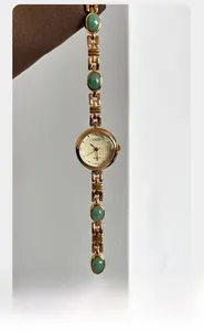 Detail of GEDI gold quartz watch with green oval gemstone inserts and textured dial