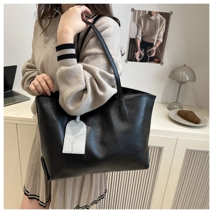 Detail of a large black vintage faux leather tote bag with a white accent charm on a model