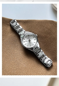 Detail of silver quartz watch with metallic link strap on textured brown fabric