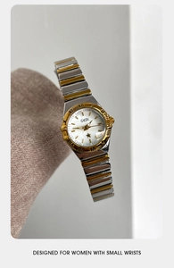 Detalle del reloj GEDI bicolor con números romanos sobre un fondo de tela rosa texturizada