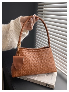 Detail of a brown woven leather tote bag featuring a thick braided handle and texture