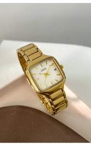 Détail d'une montre carrée dorée avec cadran blanc, guichet date et bracelet métallique