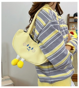 Detail of yellow crossbody bag with blue face embroidery and plush feet hanging below