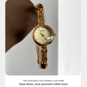 Close-up of gold chain strap watch featuring brown amber-like beads and champagne dial