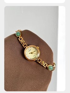 Detail of luxury gold watch with green amber stones on an elegant display stand