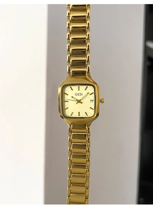 Détail macro du cadran carré doré avec guichet de date et bracelet métallique chic