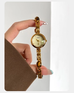 Detail of luxury gold quartz watch featuring amber stone link bracelet on female wrist
