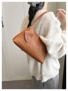 Detail of a brown woven texture shoulder bag worn by a model in soft interior light