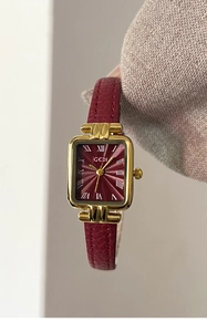 Dettaglio orologio quadrato dorato con quadrante rosso soleil e numeri romani in pelle