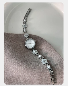 Vue détaillée d'une montre chaîne argentée avec motifs floraux et perle centrale