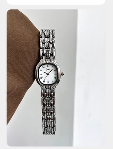 Macro shot of silver barrel-shaped watch dial with roman numerals and metallic chain strap