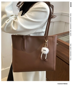 Detail of coffee brown leather tote bag with plush monster charm and sleek shoulder strap