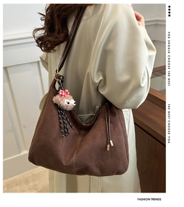Detail of a large brown suede tote bag featuring a cute plush bear pendant with bow