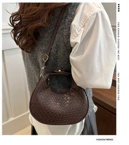 Detail of a brown woven half-moon bag featuring a metal snap closure and adjustable strap