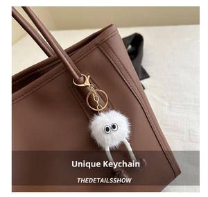 Close-up of a white plush monster charm with big eyes on a brown leather tote bag