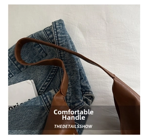 Detail shot of brown oily leather shoulder bag handles with clean stitching on denim