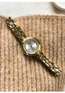 Detail of GEDI gold watch with rhinestone bezel and spiral texture strap on fabric
