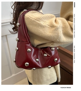 Detail view of burgundy leather underarm bag with large silver studs and curved zipper